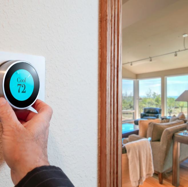 Hand adjusting a smart thermostat set to cool at 72 degrees in a modern living room.