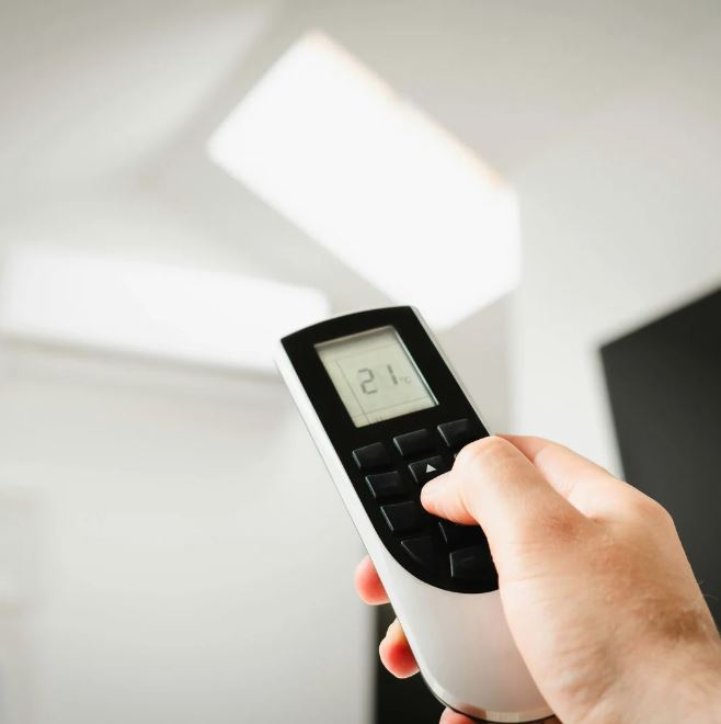 Hand holding a remote control for an air conditioning system, set to 21°C.
