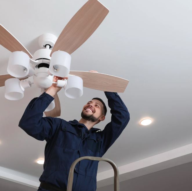 Electrician installing a ceiling fan with light fixtures.
