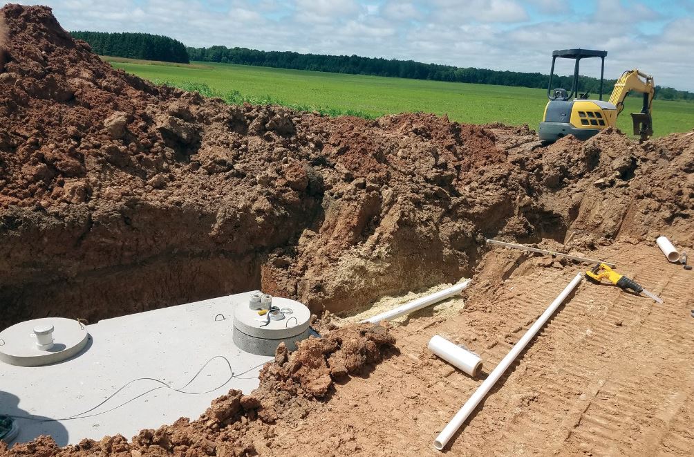 Septic tank installation in a dug-out trench with pipes and soil.