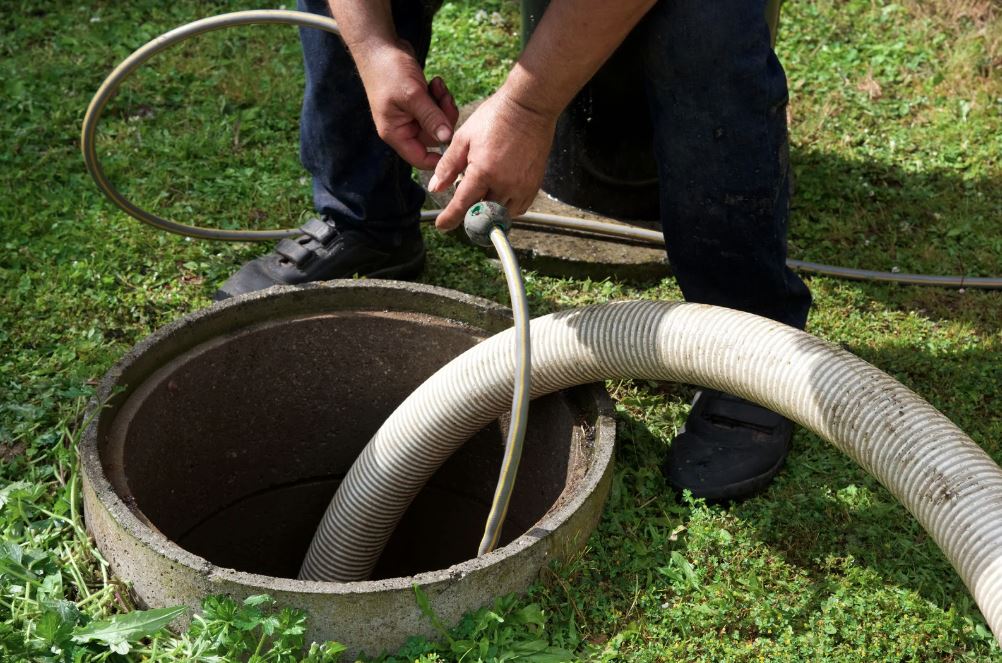 Worker inserting hose into septic tank for Sewer Line Repair in San Diego.
