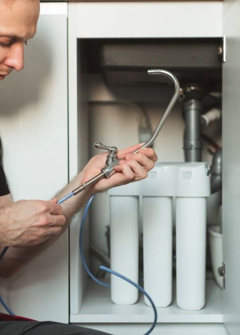 Technician installing a faucet line under sink with water filter system.