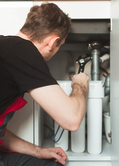 Technician servicing under-sink water filtration system with wrench.